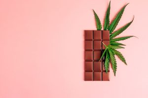 Dark chocolate and cannabis cannabis leaf on a pink background. Horizontal frame copy space top view.